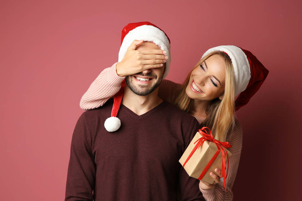 Young woman giving her boyfriend Christmas present, on color background - Zdjęcie, obraz