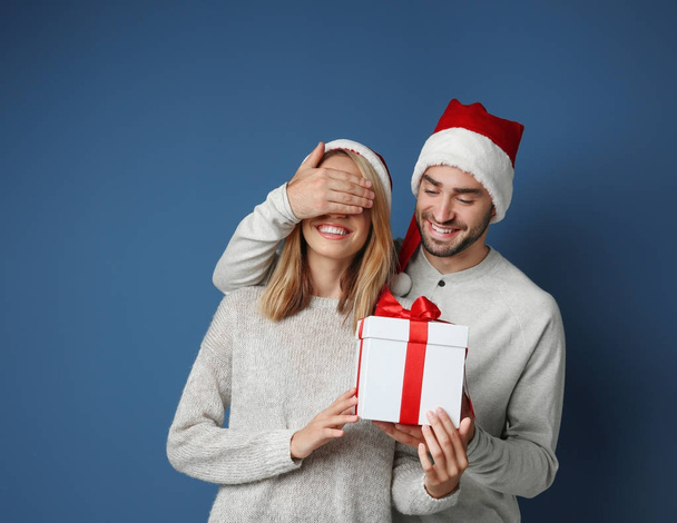 Young man giving his girlfriend Christmas present, on color background - Foto, Imagem