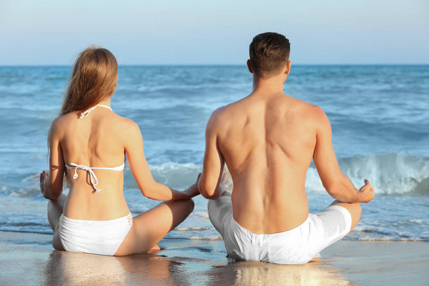 Young couple practicing yoga on sea beach - Zdjęcie, obraz