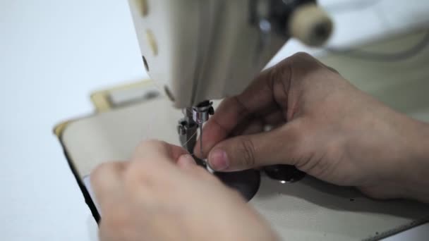 Κοντινό πλάνο του μια μοδίστρα τα χέρια βάζοντας ένα νήμα σε μια βελόνα μιας ράβοντας μηχανής - Πλάνα, βίντεο