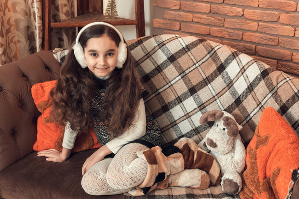 Pretty little brunette girl with long hair sitting on a sofa at  - Valokuva, kuva