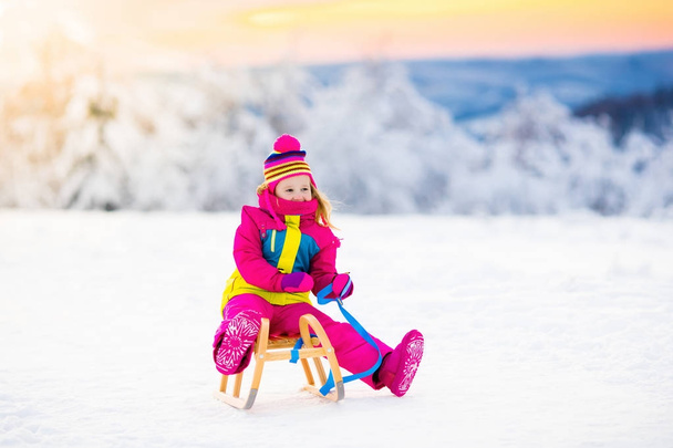 Kind spelen in de sneeuw op de slee in winter park - Foto, afbeelding