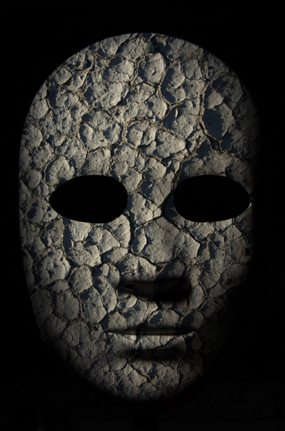 Masque texturé avec surface craquelée peinte en bois brut, expression neutre sur fond sombre
. - Photo, image