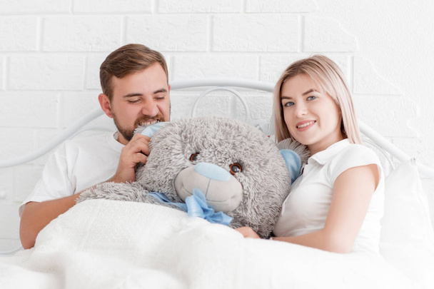 Young couple lies with a teddy bear in bed - Foto, Imagem
