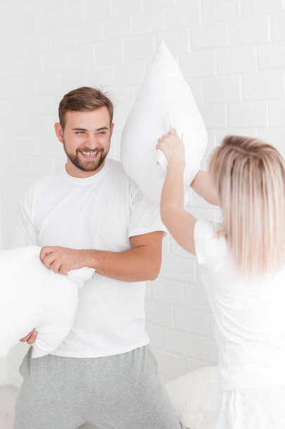 A young couple is beating pillows in the bedroom. - Zdjęcie, obraz