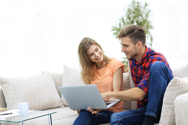 young couple is using a laptop and smiling while sitting on sofa at home - Foto, Imagem