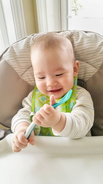 Adorable Chinese and Caucasian Baby Boy Playing With His Spoon Sitting in High Chair. - Photo, Image