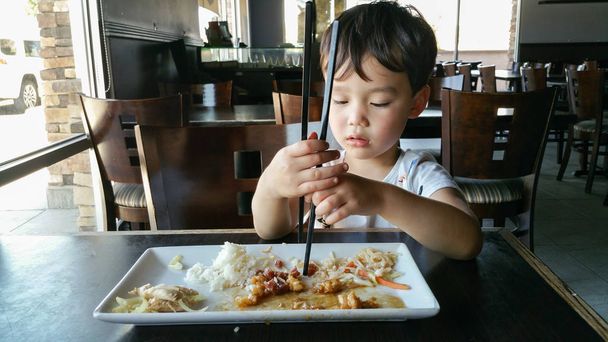Χαριτωμένα μικρά κινέζικα και Καυκάσιος αγόρι εκμάθηση της χρήσης Τσοπ στικς στο εστιατόριο. - Φωτογραφία, εικόνα