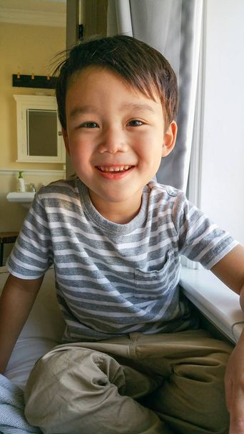 Happy Cute Young Chinese and Caucasian Boy Sitting Near Window - Photo, Image