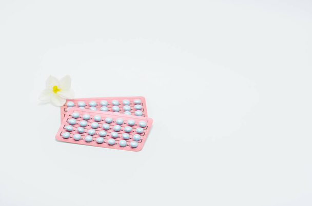 Twee blisterverpakking van hormonen voor behandeling menopauzale vrouwen en bloem op witte achtergrond - Foto, afbeelding
