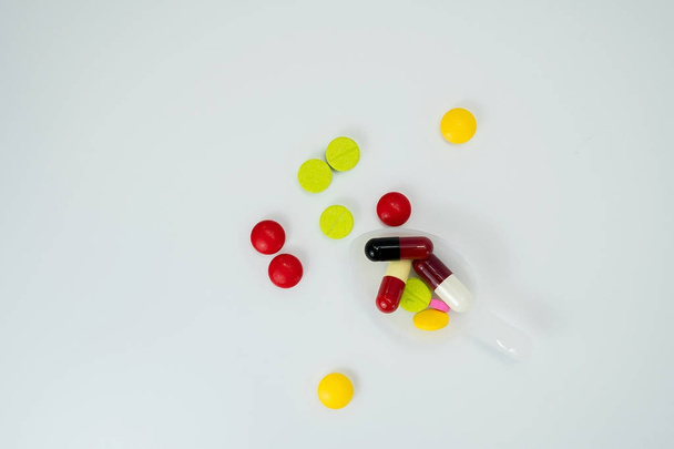 Kleurrijke tabletten in theelepel en veel pillen verspreid op een witte achtergrond met kopie ruimte - Foto, afbeelding
