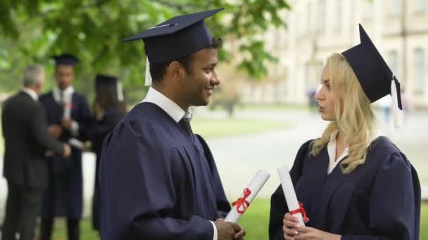 Personas con vestimenta académica y sombreros con diplomas en las manos hablando, día de graduación
 - Metraje, vídeo