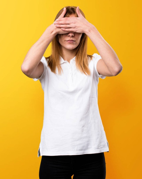 Beautiful young girl covering her eyes on yellow background - Photo, Image