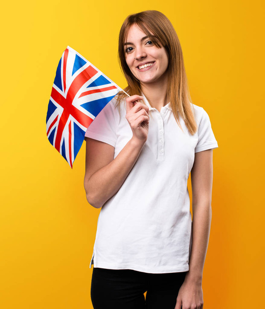 glücklich schönes junges Mädchen mit einer Flagge des Vereinigten Königreichs auf gelb - Foto, Bild