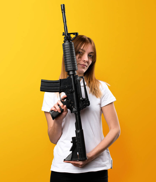 Mooi jong meisje met een geweer op gele achtergrond - Foto, afbeelding
