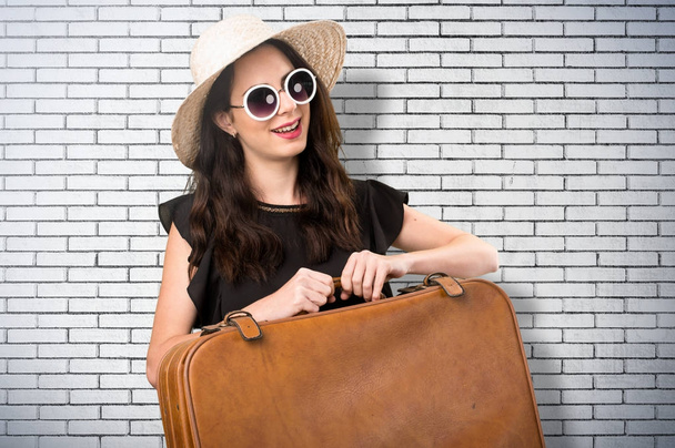 Beautiful young girl with  a suitcase on a brick wall - Fotoğraf, Görsel