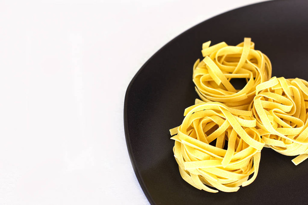 Uncooked tagliatelle on a ceramic plate. Isolated - Photo, Image