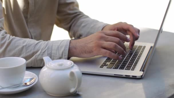 Man types something on his laptop sitting at the table in cafe - Filmmaterial, Video