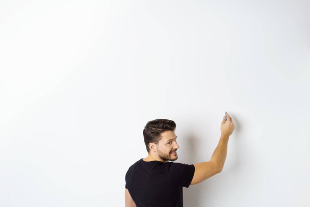Young smiling man writing on white wall - Photo, Image