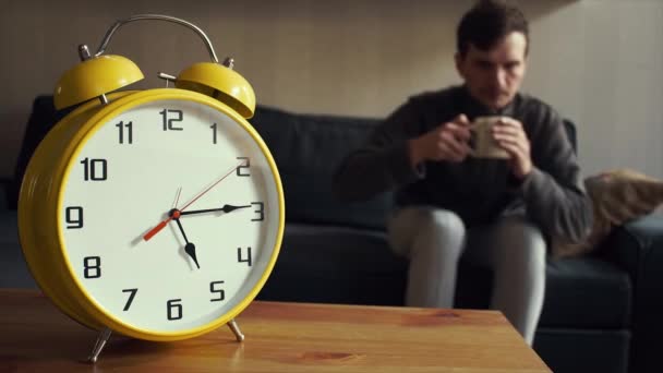 Young man puts the cup of tea on shelf. Big yellow clock is ticking - Materiaali, video