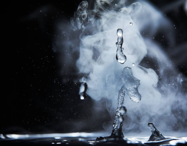 Boiling water splash with steam on black background closeup - 写真・画像