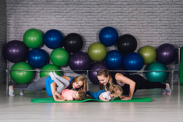 Two young sports mom and baby girls do exercises together in the - Fotó, kép