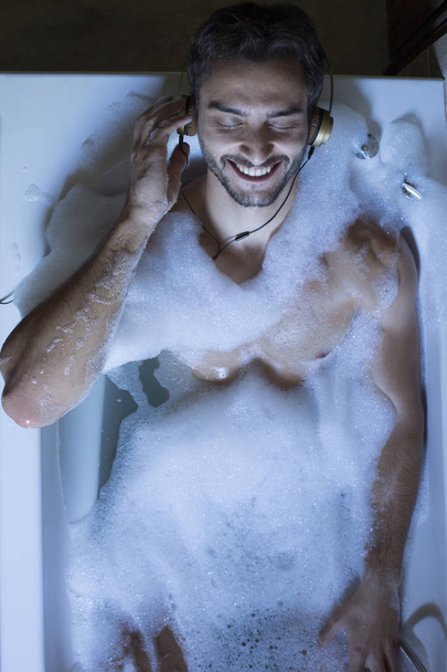naked guy in bathroom with smartphone and headphones - Zdjęcie, obraz