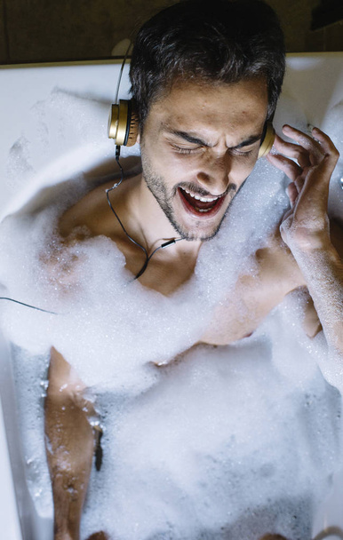 naked guy in bathroom with smartphone and headphones - Foto, afbeelding