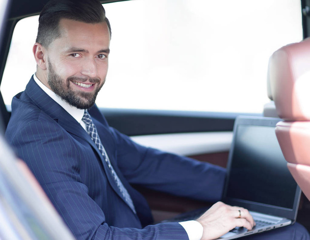 Close-up of a businessman with a laptop sitting in the car - Foto, afbeelding
