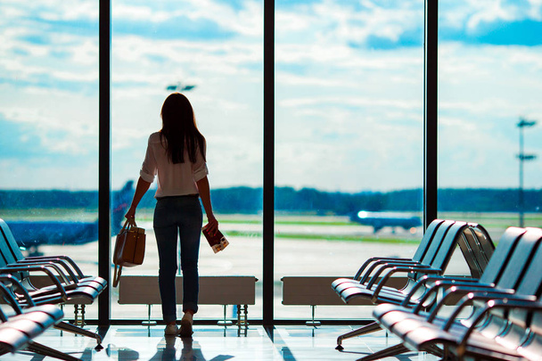 Mujer joven en el aeropuerto internacional con su equipaje fondo ventana grande. Pasajero de aerolínea en un salón del aeropuerto esperando aviones de vuelo
 - Foto, Imagen