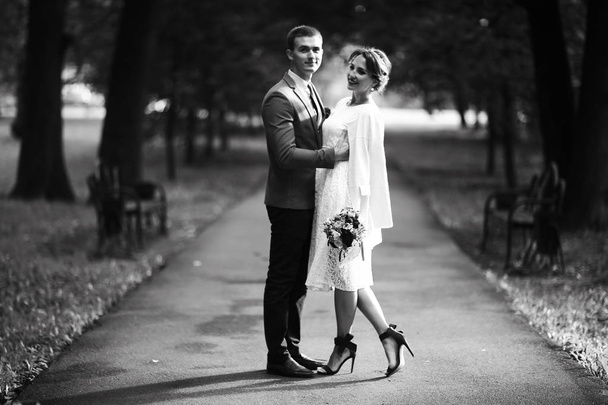 beautiful young bride in white dress and handsome groom posing in summer park on wedding day, black and white  - Photo, image
