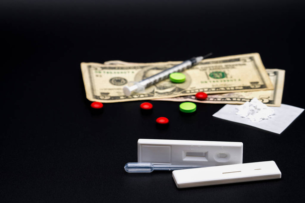 Két metamfetamin kazettás teszt műanyag Cseppentő piros és zöld gyógyszerek, hamis heroin porok, amerikai dollár számlák és fecskendő és tű a sötét háttér-val másol hely - Fotó, kép