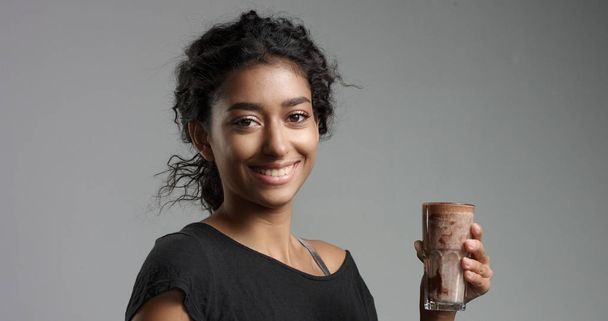 Γελώντας ελκυστικό κορίτσι Μέσης Ανατολής σε χαλαρή μαύρο top πόσιμο mocca, ζεστή σοκολάτα, σπιτικής μας παραγωγής από ένα ψηλό ποτήρι - Φωτογραφία, εικόνα