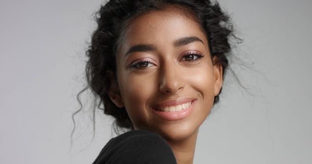 νεαρό κορίτσι με τέλεια ανοιχτό καφέ δέρμα και όμορφα σγουρά μαύρα μαλλιά χαμογελά στη φωτογραφική μηχανή - Φωτογραφία, εικόνα
