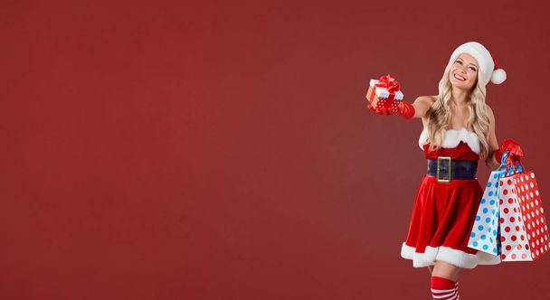 Young woman in Santa costume with packages and gift box on red C - Фото, зображення