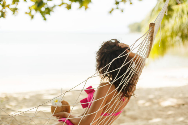 Sexy girl in a swimsuit lies in a hammock with a coconut drink - Foto, Bild