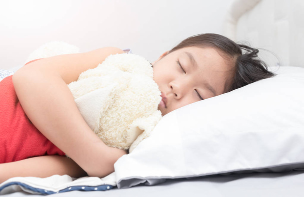 schattig klein Aziatisch meisje slapen en teddy bear knuffel op bed  - Foto, afbeelding