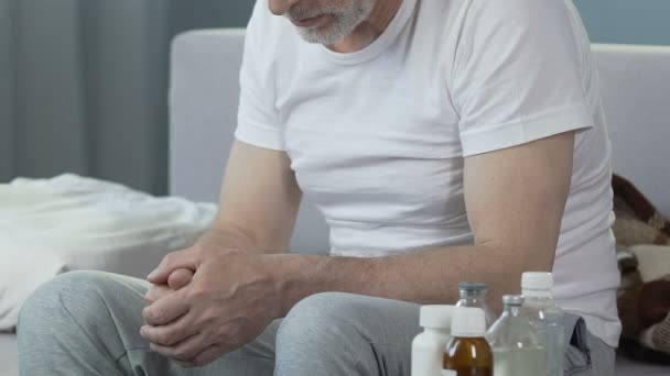 Depressed senior male sitting on bed, bottles with medicines standing nearby - Imágenes, Vídeo