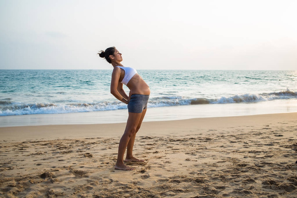 Natural looking pregnant woman practicing yoga at the seashore a - Photo, image