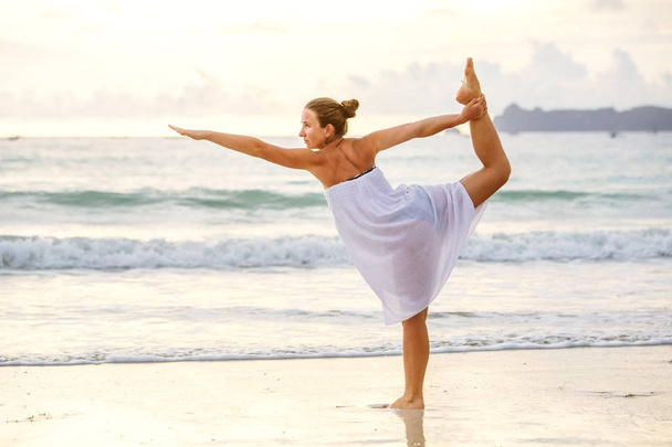 Caucasian woman practicing yoga at seashore of tropic ocean - Foto, afbeelding