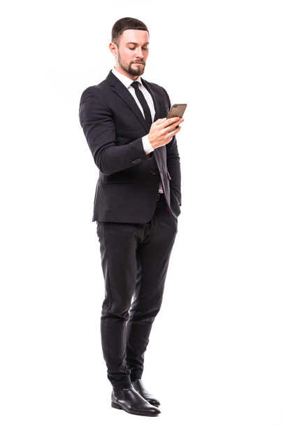 Jonge, bebaarde zakenman bericht aan het typen op het scherm van de aanraking van de smartphone. Volledige lichaam lengte portret geïsoleerd over witte studio achtergrond. - Foto, afbeelding