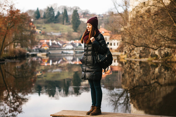 Ένα τουριστικό κορίτσι με ένα σακίδιο που στέκεται στην ακτή και απολαμβάνοντας τη φύση και την θέα από την πόλη του Cesky Krumlov στην Τσεχική Δημοκρατία. Η έννοια της σόλο ταξίδια. - Φωτογραφία, εικόνα