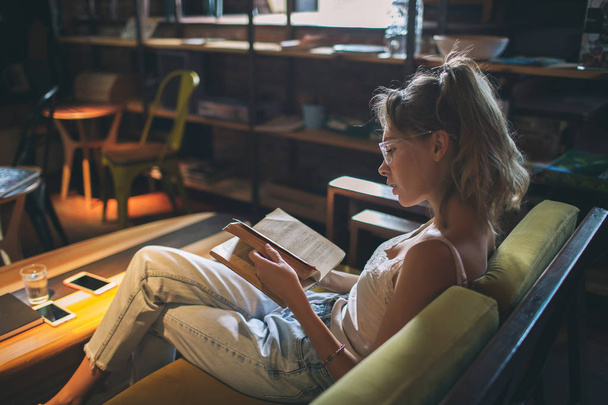 Молода красива біла жінка читає книгу в кафе в окулярах
 - Фото, зображення