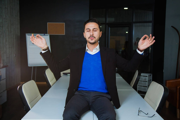 Young tired businessman meditating on office table - Photo, Image