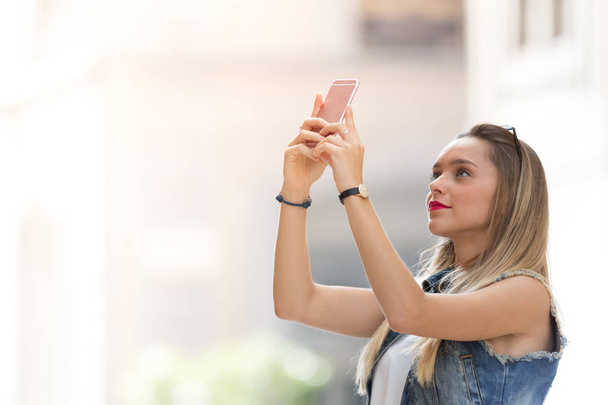 Pretty blonde teenager taking a photo with her mobile phone - Photo, Image