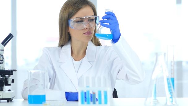 Женщина-исследователь, изучающая голубое решение во фляжке в лаборатории
 - Фото, изображение