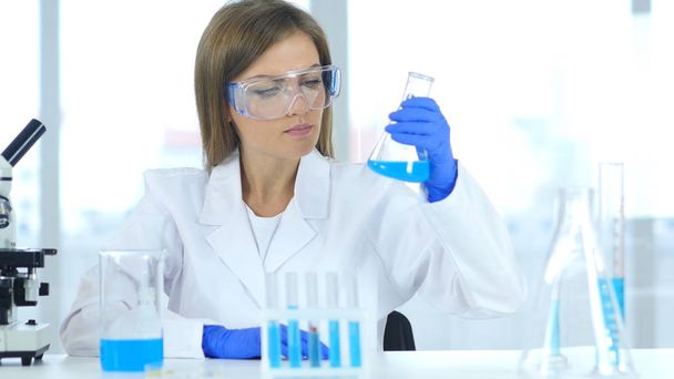 Female Scientist Looking at Results of Reaction in Flask in Laboratory - Foto, Imagen