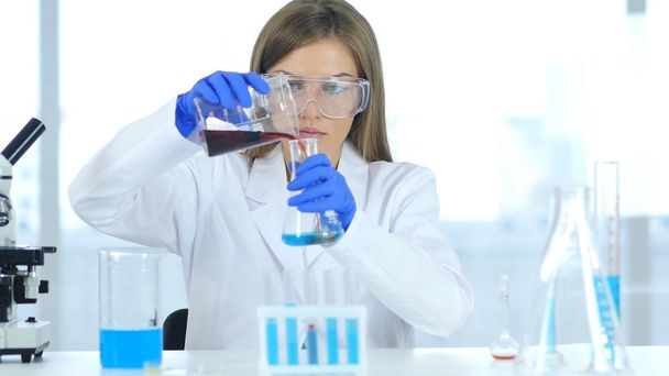 Científica femenina trabajando en laboratorio, vertiendo solución química en tubo de ensayo
 - Foto, Imagen