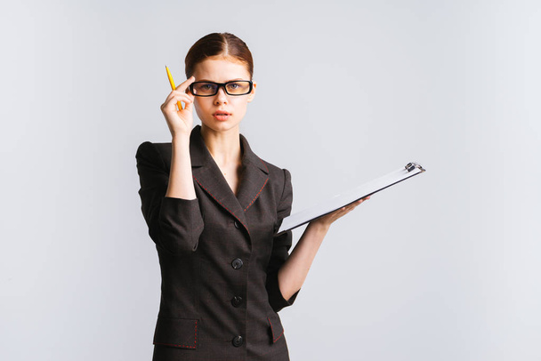 attentive business lady in a black suit is holding a folder and a pen, holding her glasses and looking directly at the camera - Foto, immagini