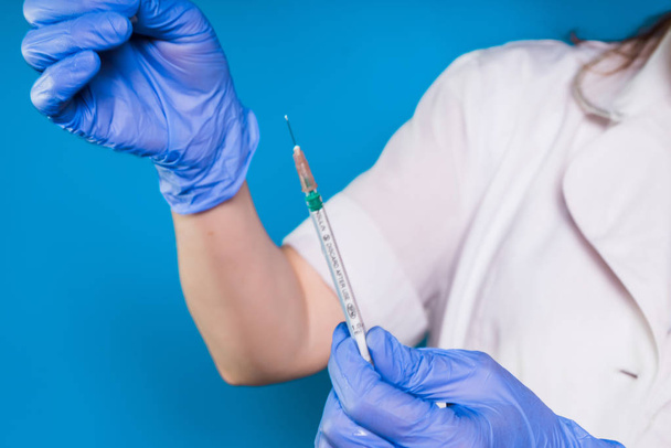 nurse holding a prick in gloves, a syringe close-up, isolated on a blue background - Photo, Image